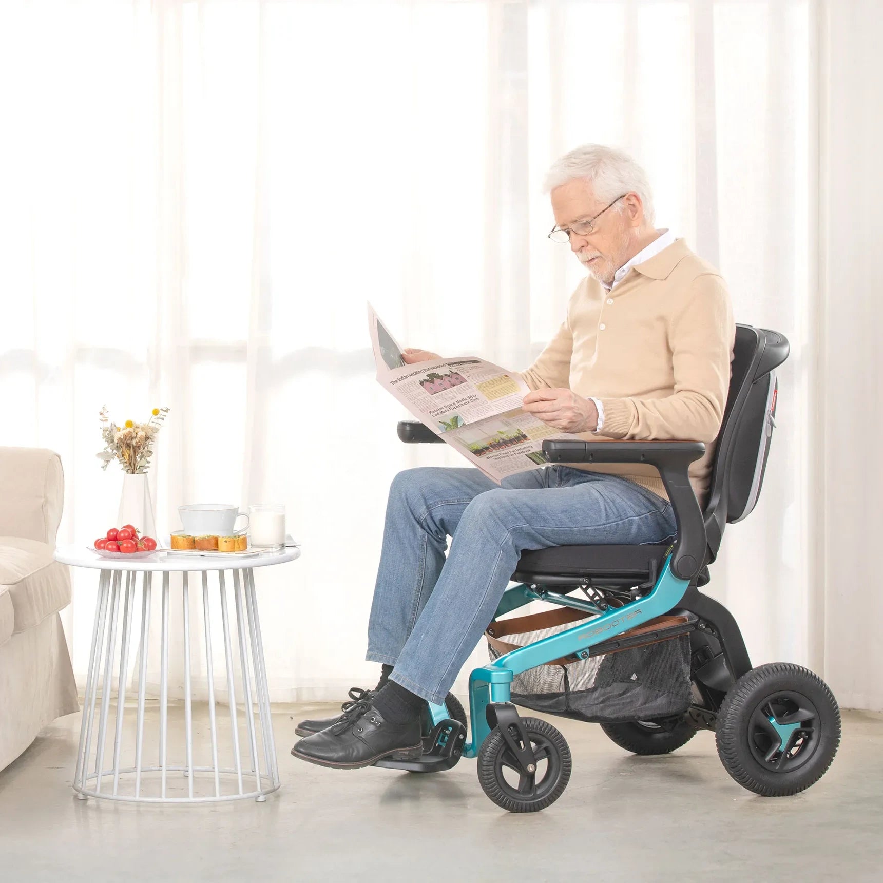 Senior man reading a newspaper while seated in a teal Robooter E40 power wheelchair at home